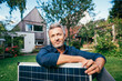© Westend61 - Smiling mature man sitting with solar panel in front of house