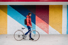Man Wheeling Bicycle In Front Of Colorful Wall