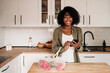 © Westend61 - Smiling woman holding smart phone with mesh bag on kitchen island at home