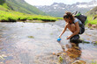 © Antonioguillem - Hiker filling canteen with raw water in a river