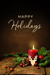 Grußkarte, Weihnachtskarte mit englischem Text Happy Holidays. Dekoration mit roter Kerze, Tannenzweigen, Zapfen, Kugeln und Rentier auf Holz. Hochformat.