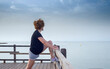 An adult woman practices stretching and yoga postures on a pier by the sea.