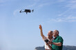© alex.pin - coppia di anziani si diverte con un drone che pilotano in volo in una spiaggia con il cielo blu