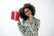 Leinwanddruck Bild - Portrait of young attractive african american woman with curly hair and glasses presenting gift box in studio on white background.