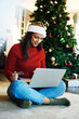 © N F/peopleimages.com - Christmas, laptop and woman use credit card for payment, happiness or ecommerce for festive season in lounge. Xmas, young female or device for online banking, peace or relax with transaction on floor