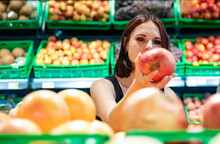 Young Woman In Supermarket Choosing Pomegranate Fruits