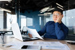 © Liubomir - Serious thinking asian man working with documents inside office, concentrated businessman with contracts and bills reading and calculating reports, mature financier with documents.