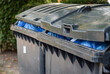Seitliche Nahaufnahme von zwei mit blauen Müllsäcken randvoll gefüllten Mülltonnen – selektiver Fokus