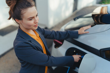 Wall Mural - Young woman charging her electric car in home, sustainable and economic transportation concept.