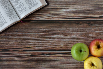 Wall Mural - Open Holy Bible Book and three apples in various colors on wooden background with copy space. Top table view.