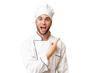 Young handsome chef man over isolated background surprised and pointing side