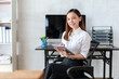 © amnaj - Attractive Asian business woman sitting at work happily working using tablet at office and smiling comfortably.