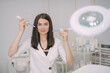 © Anna - Portrait of a young beautiful woman beautician in a medical white uniform in her office with cosmetology equipment