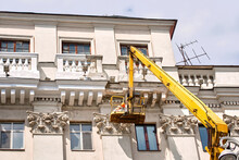 Worker Repairing Balcony, Historic Architecture Of Old Building Facade. Plaster Cladding And Crack Repairs. Plasterer Repair Cracked Balcony At Height, Renovation Work. Worker Work In Lifting Bucket