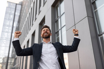 Wall Mural - Happy successful young european male manager with beard in suit makes victory gesture