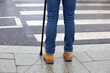 © Oleg - Man standing with walking cane on crosswalk. Male legs in jeans in front of pedestrian crossing, street safety