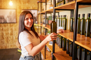 portrait of a smiling mid age latin woman holding a bottle of olive oil from the shelves in the store