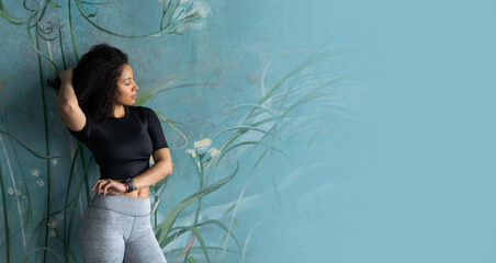 Wall Mural - Middle-aged curly black woman posing over painted green plant blue background. Looking to right. Copy space, mock-up. Eco natural, environment conservation positive winter concept.