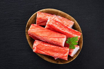 Poster - Crab sticks and parsley in a wooden bowl on dark background. Top view.