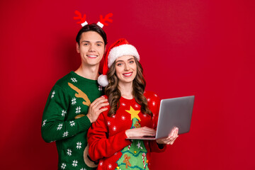 Sticker - Portrait of two positive people hug embrace use netbook santa headwear deer antlers isolated on red color background