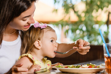 Wall Mural - Woman mom feed toddler girl with salad