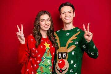 Poster - Photo of positive couple wife husband wear ugly sweaters demonstrate v-sign rejoice time together weekend isolated on red color background