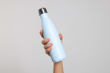 Wall Mural - Woman holding thermo bottle of drink on light background, closeup