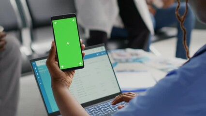 African american woman holding smartphone with greenscreen, using chroma key display in hospital reception. Person looking at isolated copyspace with mockup background, waiting room.