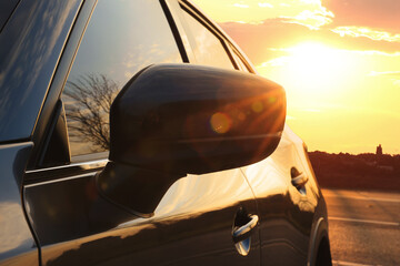 Wall Mural - Black modern car parked on road at sunset, closeup of side view mirror