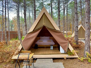 Huge tent with a double bed and a table with two chairs in front of the tent in the forest