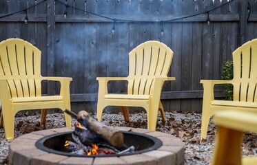 Wall Mural - Fire pit with fire-burning logs, surrounded by yellow plastic chairs, in the backyard