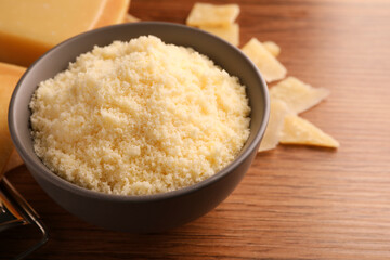 Delicious grated parmesan cheese in bowl on wooden table, closeup