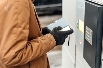 Wall Mural - A man with a phone in his hands near the self-service mail terminal. Parcel delivery machine. Person holding a smartphone. Mail delivery and post service, online shopping, e commerce concept