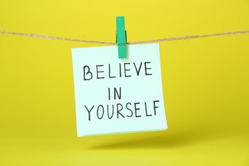 Wall Mural - Card with phrase Believe In Yourself hanging on rope against yellow background. Motivational quote