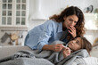 © DimaBerlin - Worried mother checking measuring temperature of sick child daughter lying under blanket at home, anxious mom looking at thermometer, taking care about unwell ill kid with high fever resting in bed