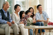 three generation asian family sitting on couch watching tv together at home