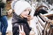 © Анна Молько - a cute little girl in a white hat on a background of snowy trees shows a peace sign