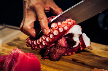 Close up of Chef cook hands chopping octopus for traditional Asian cuisine with Japanese knife. Professional Sushi chef cutting seafood japanese chefs are making octopus sashimi. Dark Tone