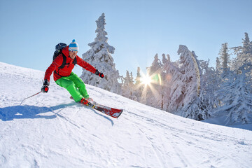 Wall Mural - Skier skiing downhill in high mountains against against the fairytale winter forest with sunset.