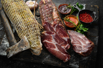 Wall Mural - Dried and salted piece of meat. Prosciutto, jamon, on a black stone background. Top view. Free space for text.