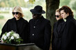 Group of people standing by coffin at funeral ceremony outdoors all wearing black with sunglasses, copy space