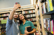 © AntonioDiaz - Smiling man and woman posting a selfie on social media while at the book shop