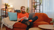 © Andrii Iemelianenko - Handsome redhead man freelancer at home living room sitting on orange couch, opens laptop start working. Young guy works on notebook, sends messages, makes online purchases, watching movies, working