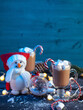 Two hot cocoa with marshmallows and candy cane on a blue table and a snowman in a Santa Claus hat. Vertical postcard copy space