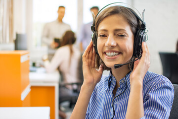 Wall Mural - Portrait of beautiful friendly female customer services agent with headset working in call center.