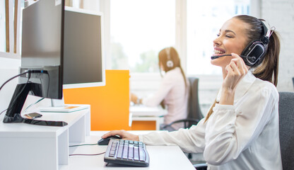 Wall Mural - Happy smiling female customer service operator working on computer in office.