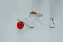 Teenage Girl Stepping On Red Christmas Ornament Against White Background