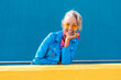 © VISTA by Westend61 - Happy woman wearing sunglasses in front of blue wall