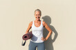 © VISTA by Westend61 - Smiling woman with yoga mat in front of cream colored wall