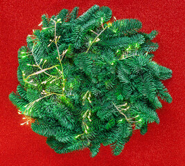 Wall Mural - christmas tree branches with golden lights garland on a festive red shiny background top view, copys